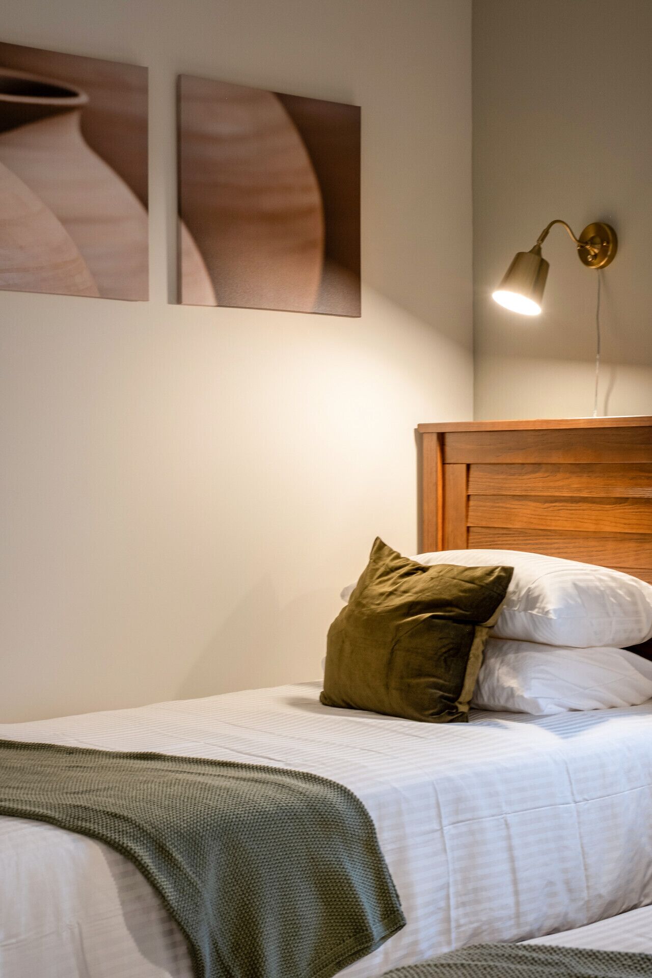Ein ordentlich bezogenes Bett mit einem Holz-Kopfstück, einer grünen Tagesdecke und zwei Kissen.