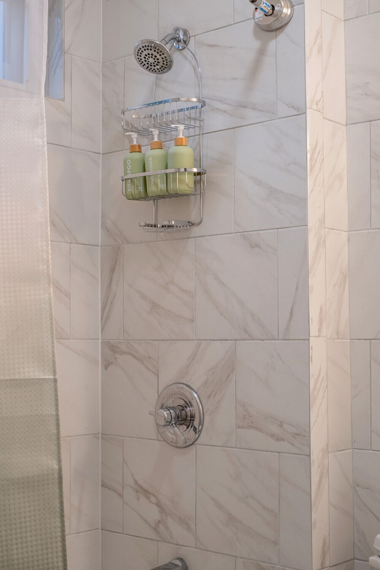Un baño con ducha, dispensador de jabón en la pared y un perchero para toallas.