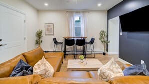 A living room with a sofa, coffee table, and a dining area with chairs and a table. - Sleek Escape: Modern 3 BR- 4 Min from West Point ! (Highland Falls)