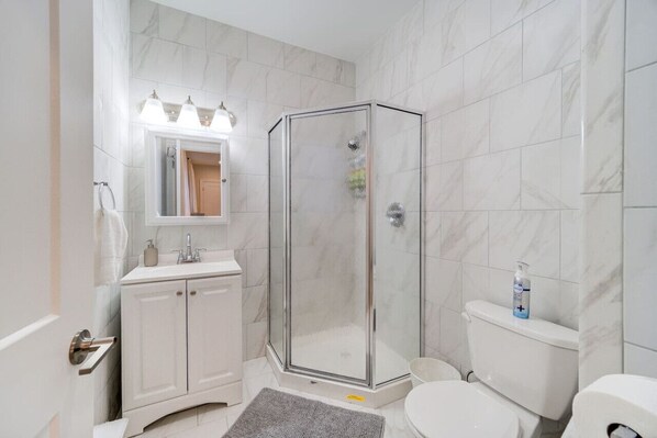 Un baño con cabina de ducha de vidrio, un lavamanos blanco con espejo y un inodoro.