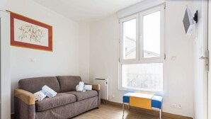 A room with a brown sofa, a small table, and a window. - Elegant Studio - 2P - Malakoff (Malakoff)