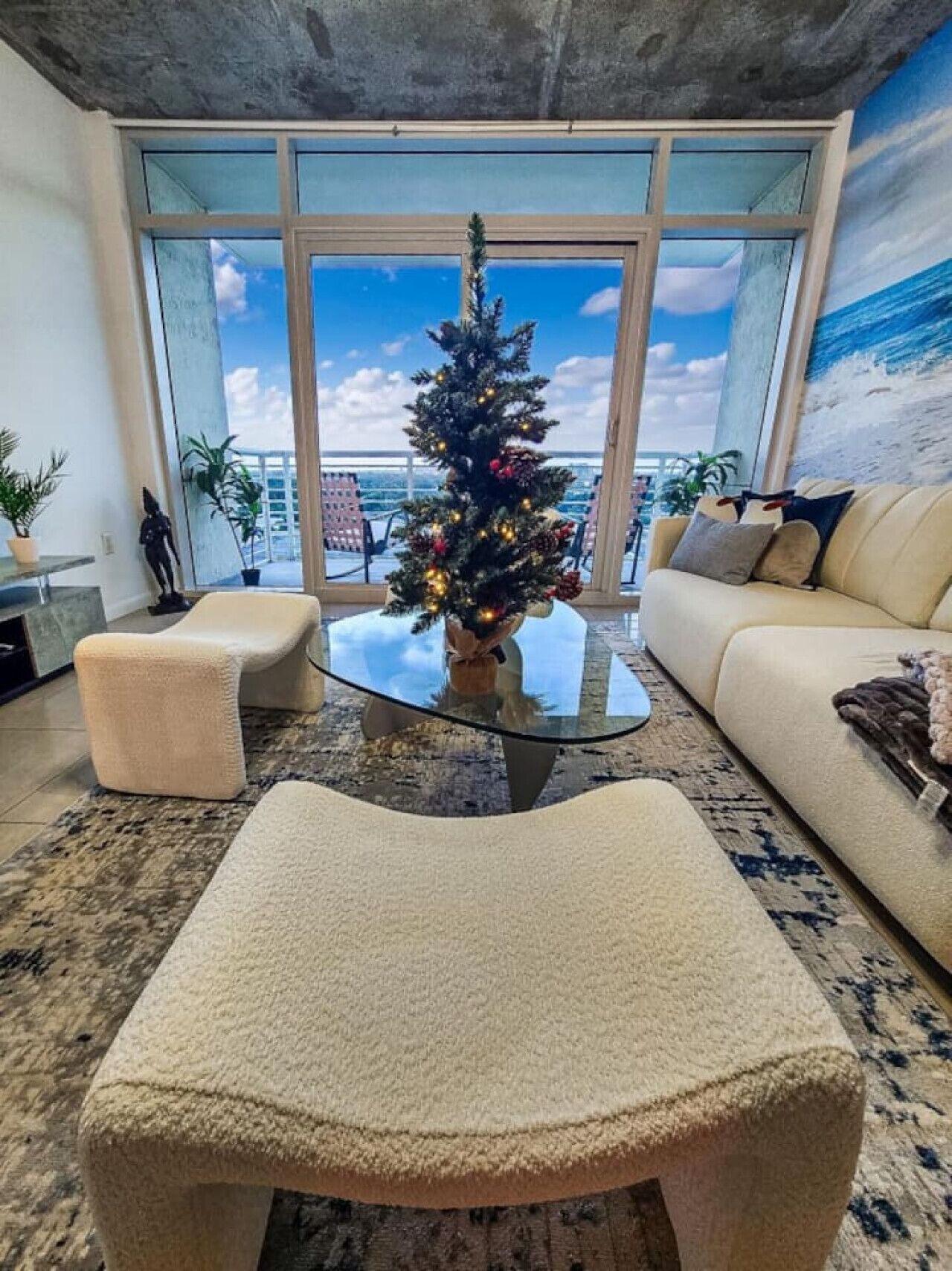 A modern living room with a glass coffee table, a Christmas tree, and a sofa.