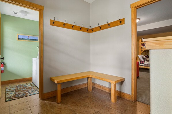 Una habitación de esquina con un banco de madera, un perchero y una puerta que da a otra estancia.