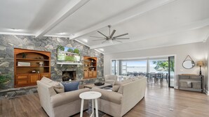 A modern living room with a stone fireplace, a ceiling fan, and a view to the outdoors. - Lakeshore Lookout - Amazing Long Range Views, Pool, Hot Tub, Fire Pit, Theatre Room and much more! (Mooresville)
