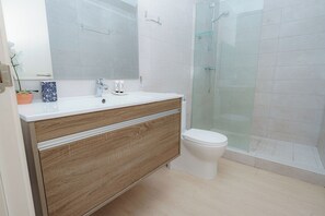 Une salle de bain moderne avec un meuble-lavabo en bois, un lavabo blanc et une cabine de douche en verre.