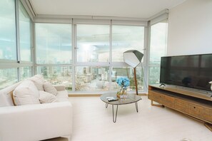 A modern living room with a white sofa, a coffee table with decorative items, a floor lamp, and a TV on a wooden cabinet.