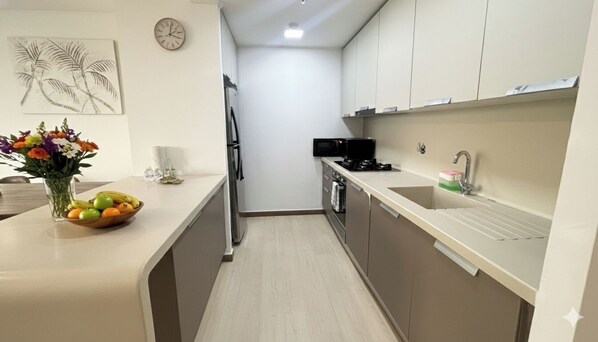 A modern kitchen with a microwave, stove, and sink. There is a clock on the wall and a vase with flowers on the counter.