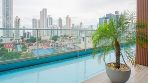 A rooftop pool with a cityscape view, a palm tree planter, and a glass railing.