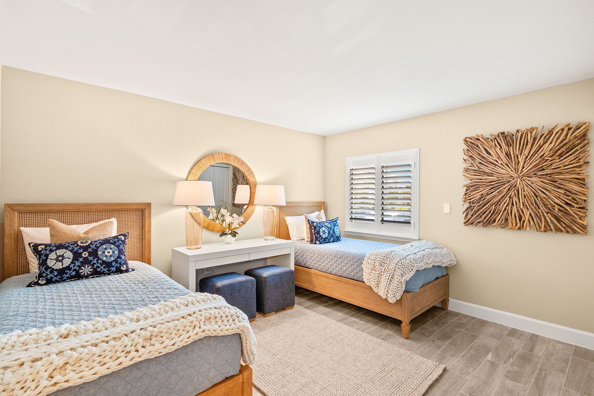 A bedroom with two beds, a bedside table with lamps, a mirror, and a decorative wall piece.