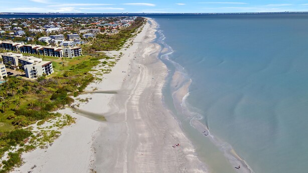 Vista aérea de una zona costera con playa de arena, una hilera de edificios de varios pisos y una vista despejada del océano.
