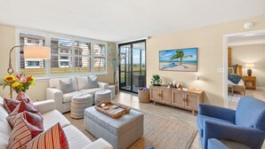 Una sala de estar moderna con un sofá, un reposapiés y un sillón azul, un mueble de madera y un cuadro de una escena de playa.