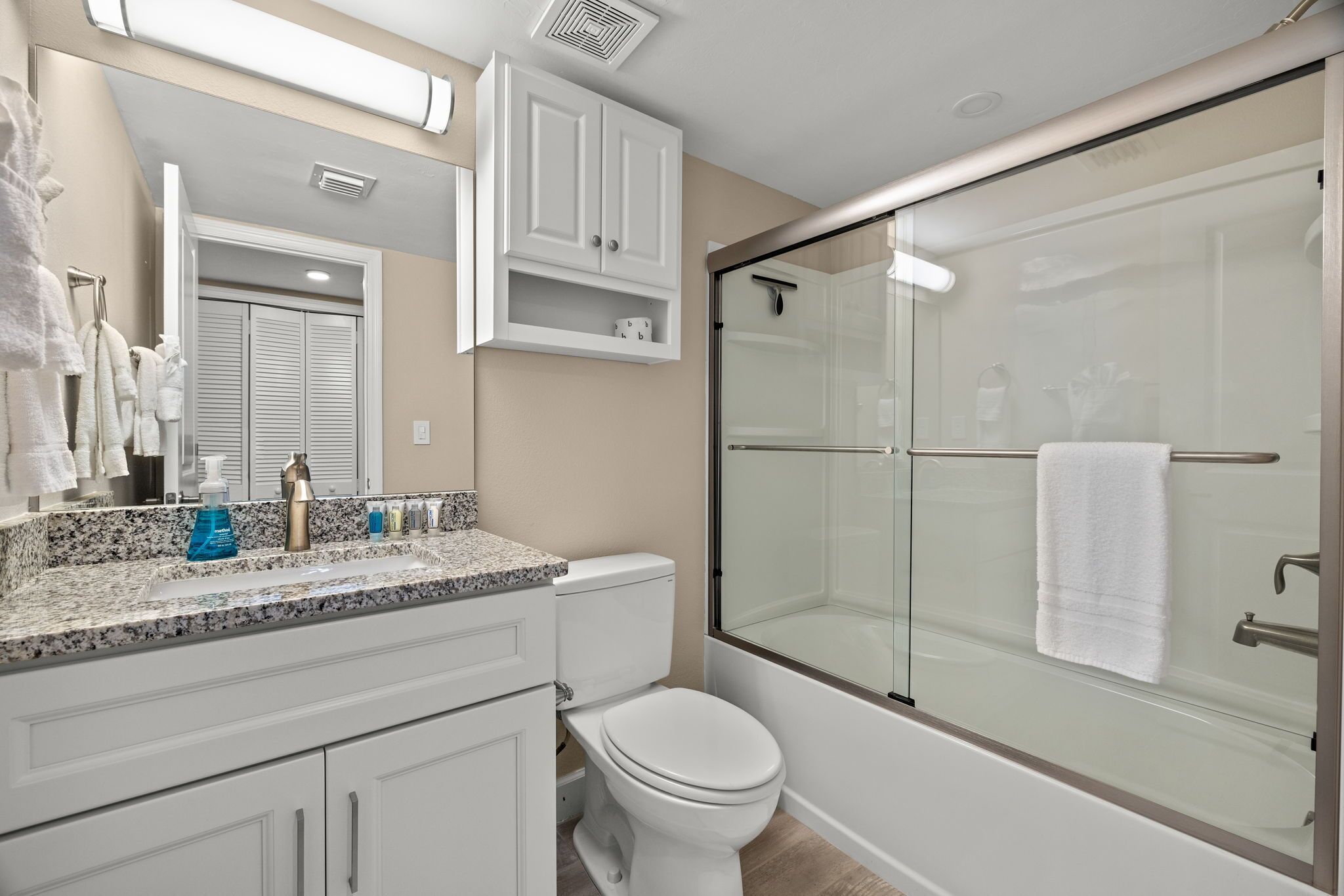 A modern bathroom with a glass-enclosed shower, a white toilet, and a granite countertop with toiletries.