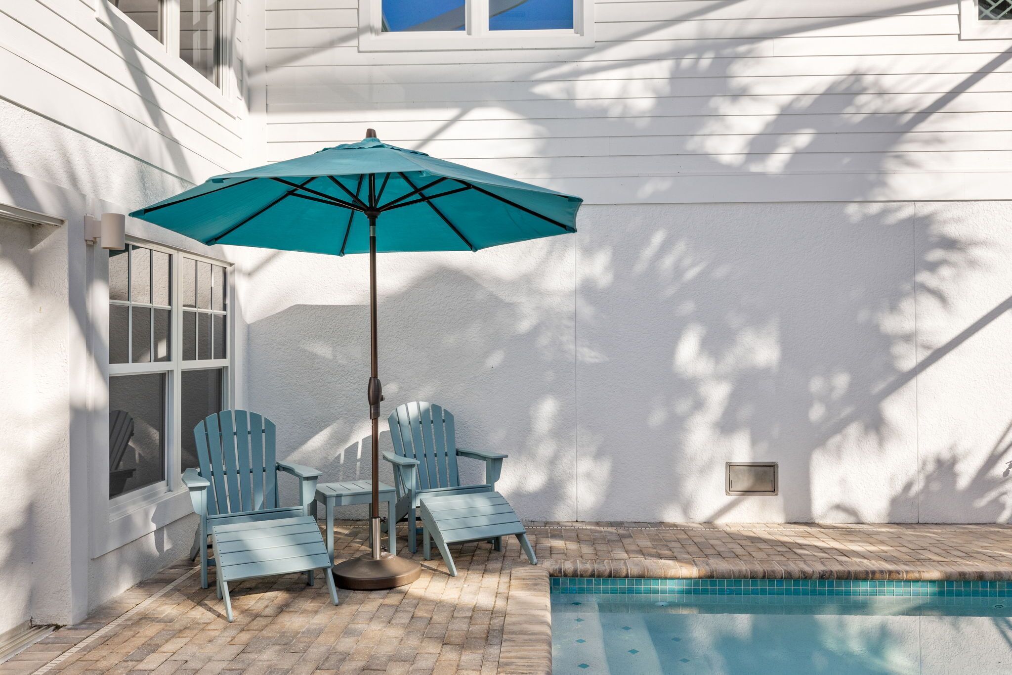 Un patio con piscina, dos sillas tipo Adirondack y un paraguas turquesa.