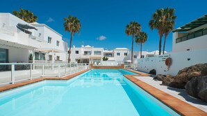 A swimming pool with a clear blue water, surrounded by white buildings and palm trees. - Lanzahost Tabaiba Green (Costa Teguise)