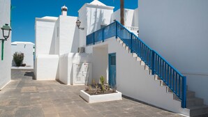 A narrow alleyway with white buildings, a blue staircase, and a small garden area. - Lanzahost Tabaiba Green (Costa Teguise)
