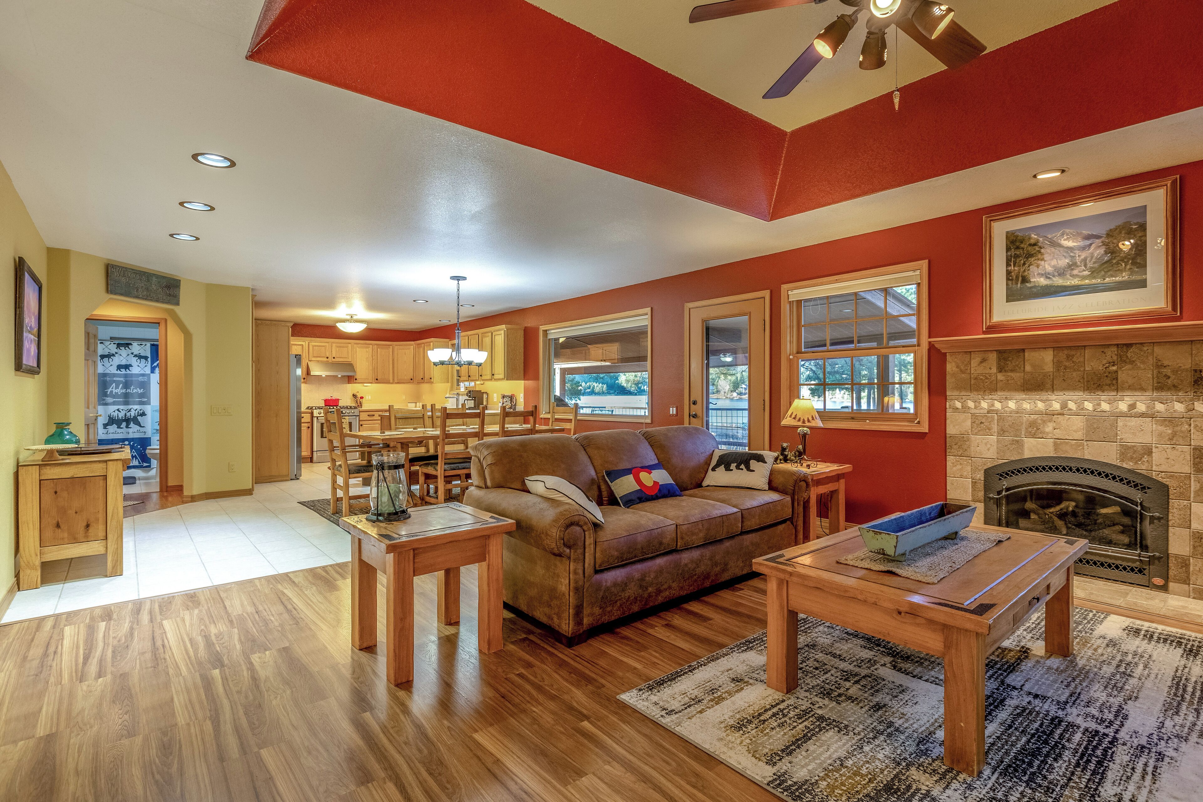 A spacious living room with a fireplace, wooden furniture, and a view of the kitchen.