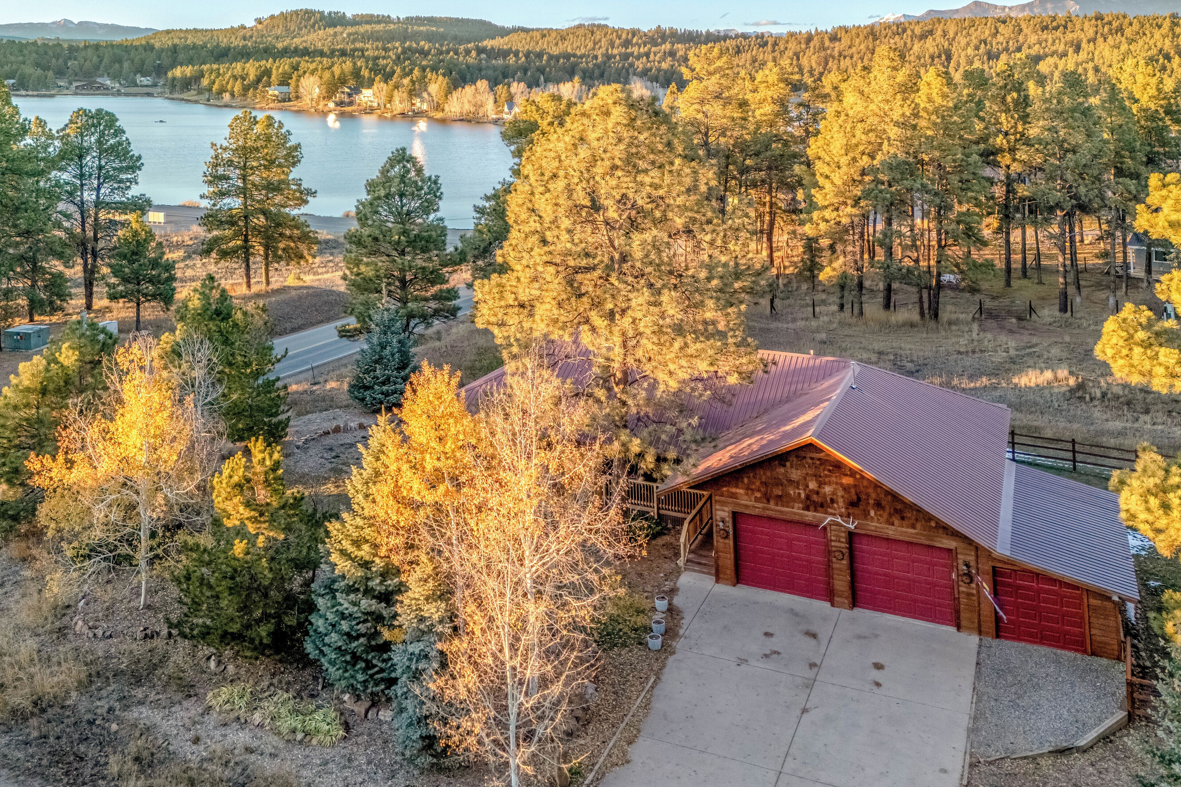 A cabin with a red garage, surrounded by trees and a lake.