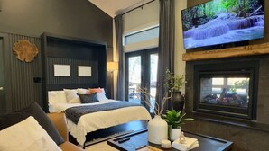 Una habitación de hotel moderna con cama, sofá, televisión y chimenea.