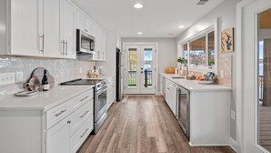 A modern kitchen with white cabinetry, a wooden floor, and a view through a glass door to the outside. - Azalea Point by SoCharm | Quaint Lakefront Retreat (Sherrills Ford)