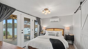 A bedroom with a bed, bedside tables, a ceiling light, and a view of a lake through glass doors. - Azalea Point by SoCharm | Quaint Lakefront Retreat (Sherrills Ford)