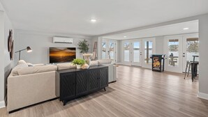 A spacious living room with a beige sofa, a dark wooden cabinet, and a large window with a view of the outdoors. - Azalea Point by SoCharm | Quaint Lakefront Retreat (Sherrills Ford)