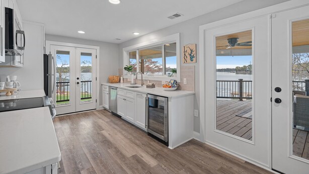 A modern kitchen with white cabinets, a stainless steel oven, and a large window overlooking a deck. - Azalea Point by SoCharm | Quaint Lakefront Retreat (Sherrills Ford)