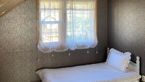 Une chambre avec un lit superposé en bois, une fenêtre avec des rideaux légers et un mur à texture.