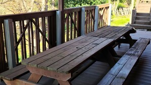 Une table de pique-nique en bois est installée sur une terrasse extérieure, dotée d’une rambarde en métal et d’un escalier menant à une zone herbeuse.