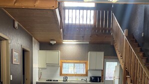 Un intérieur chaleureux avec un canapé, une table à manger, des chaises, un coin cuisine et un escalier en bois.