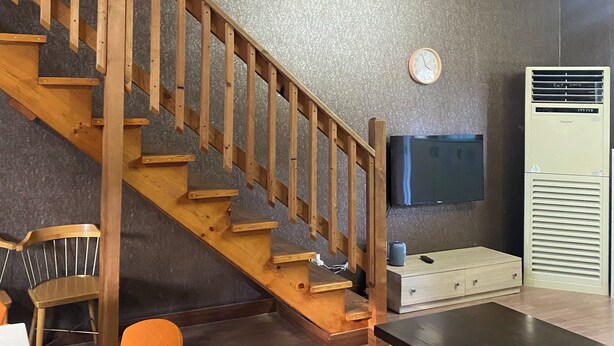 Un escalier avec des rampes en bois mène à un niveau supérieur. Un téléviseur à écran plat est fixé au mur au-dessus de l’escalier.