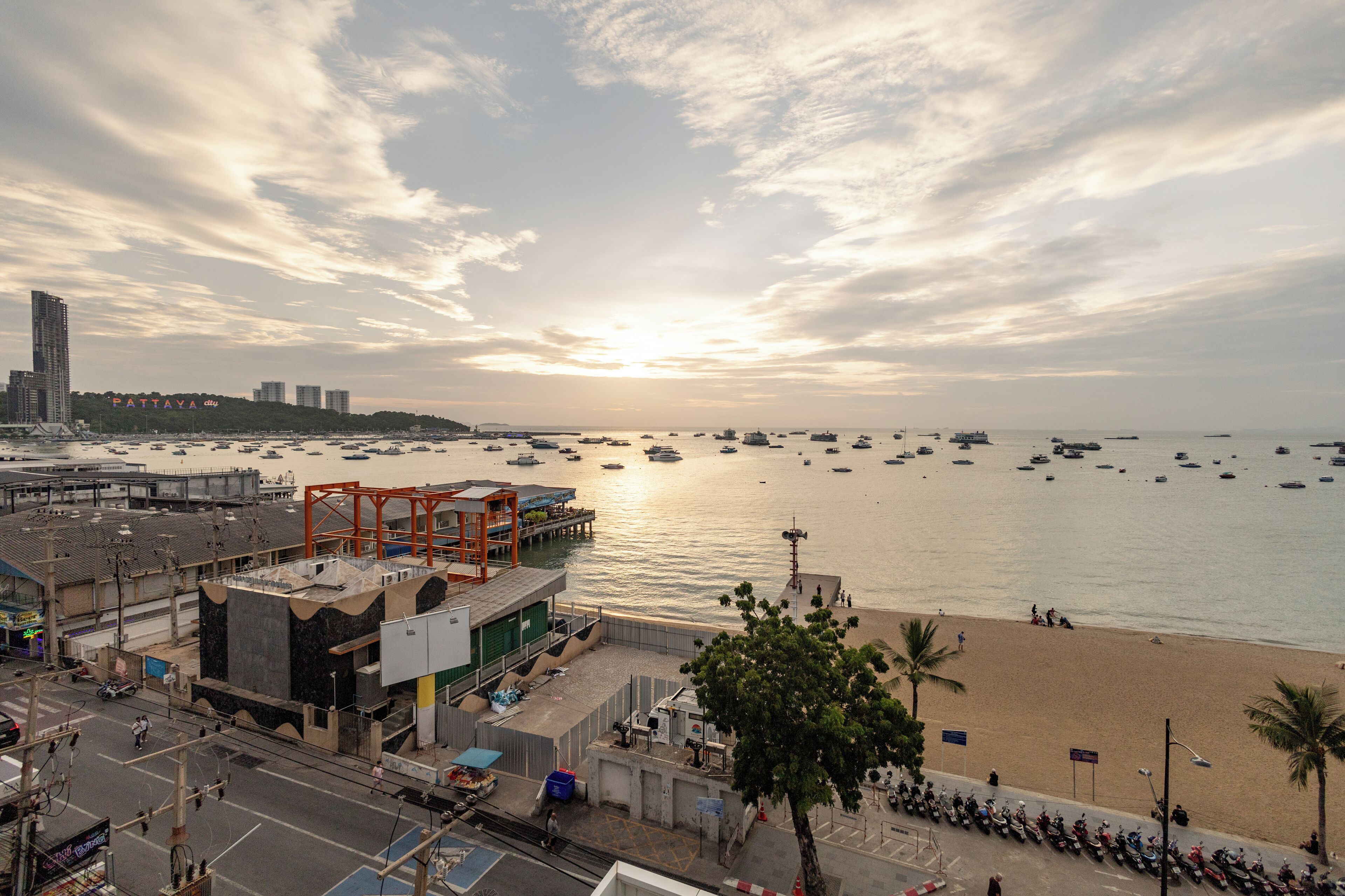 A coastal cityscape with a beach, boats, and a large orange structure.