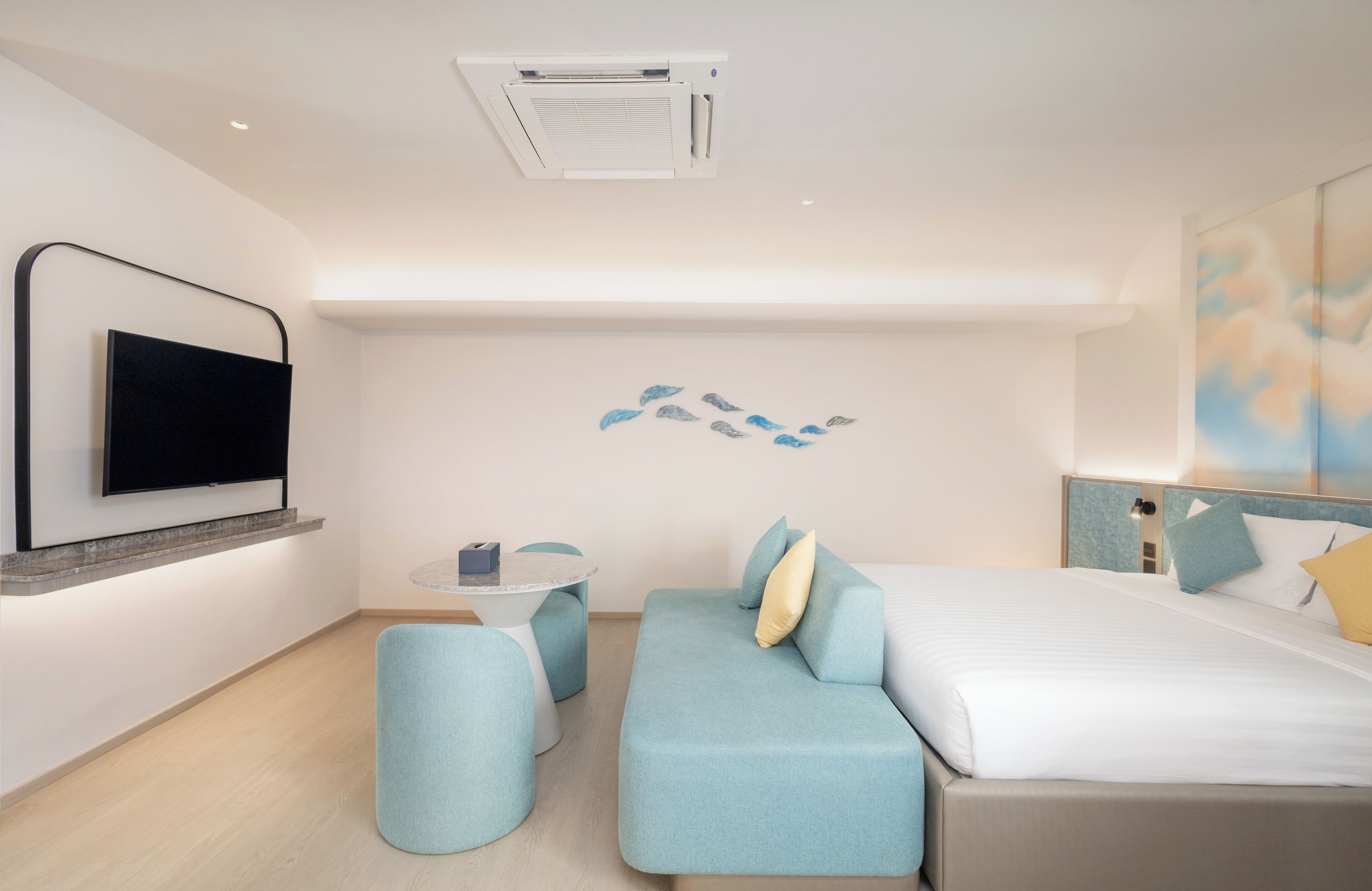 Ein modernes Hotelzimmer mit einem Wand-Fernseher, einem Sofa, einem Bett und einem kleinen runden Tisch.