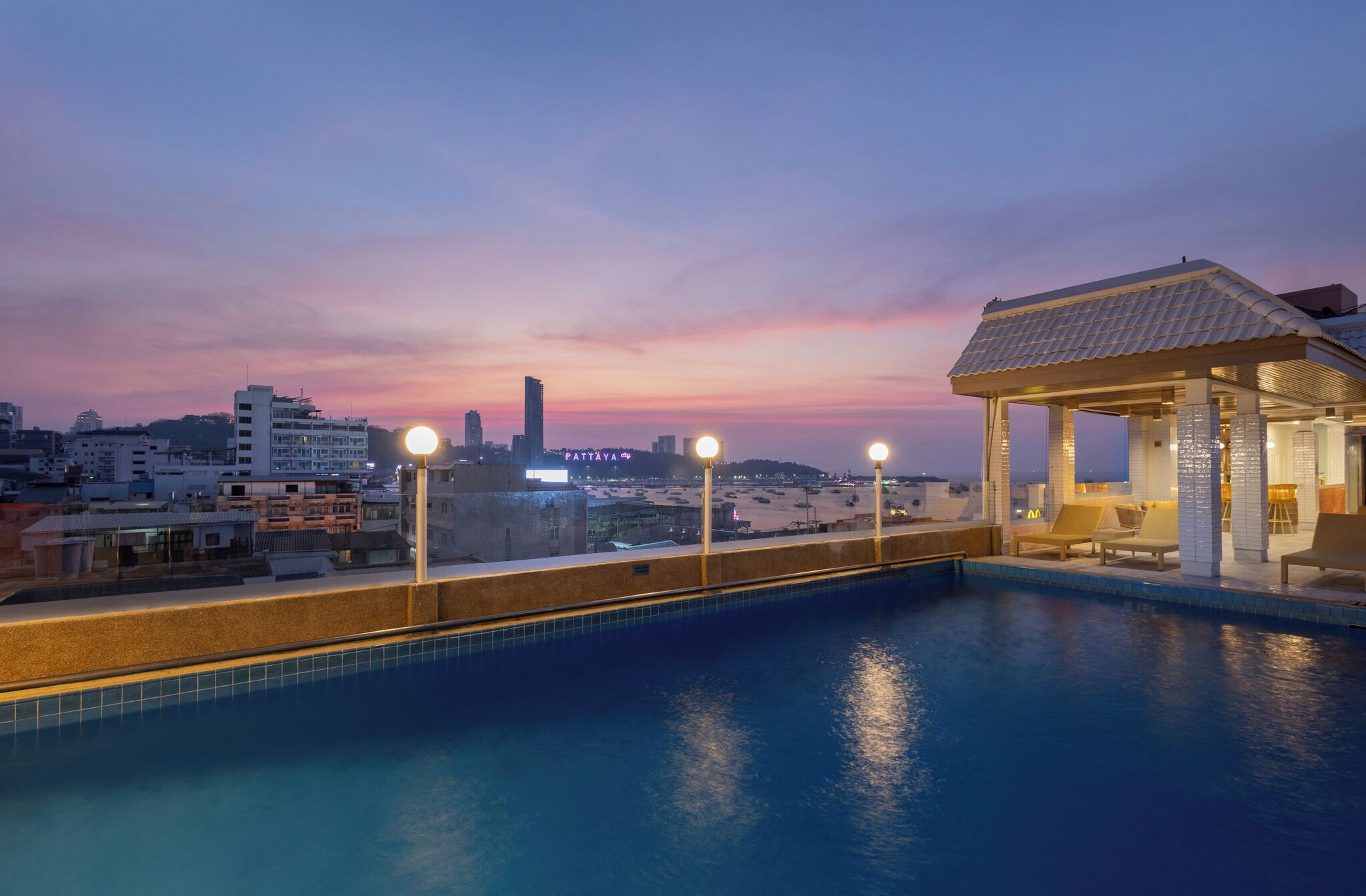 A rooftop swimming pool with a view of a city skyline at dusk.