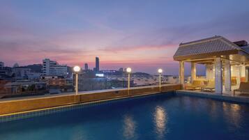 A rooftop swimming pool with a view of a city skyline at dusk.