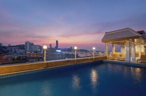 Une piscine sur le toit d’un immeuble, offrant une vue sur les toits de la ville au crépuscule.