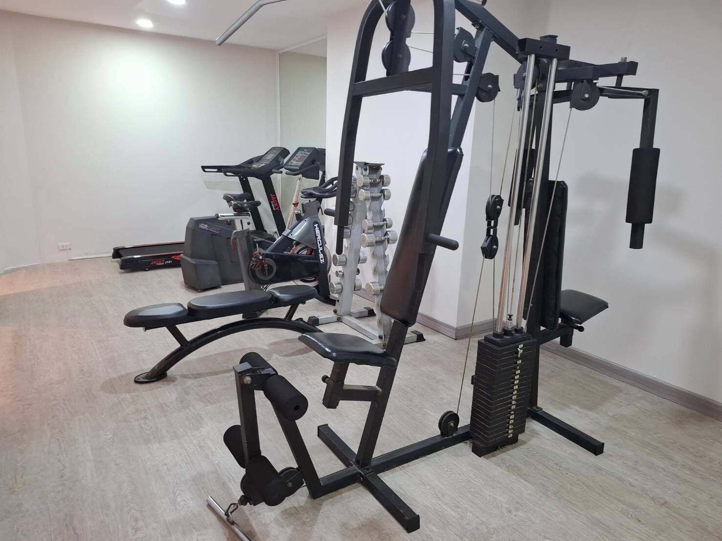 A gym with various exercise equipment including a bench press, a cable machine, and a stationary bike.