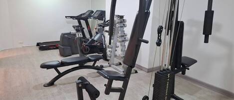 Un gimnasio con varios equipos de ejercicio, incluyendo una prensa de banca, una máquina de poleas y una bicicleta estática.