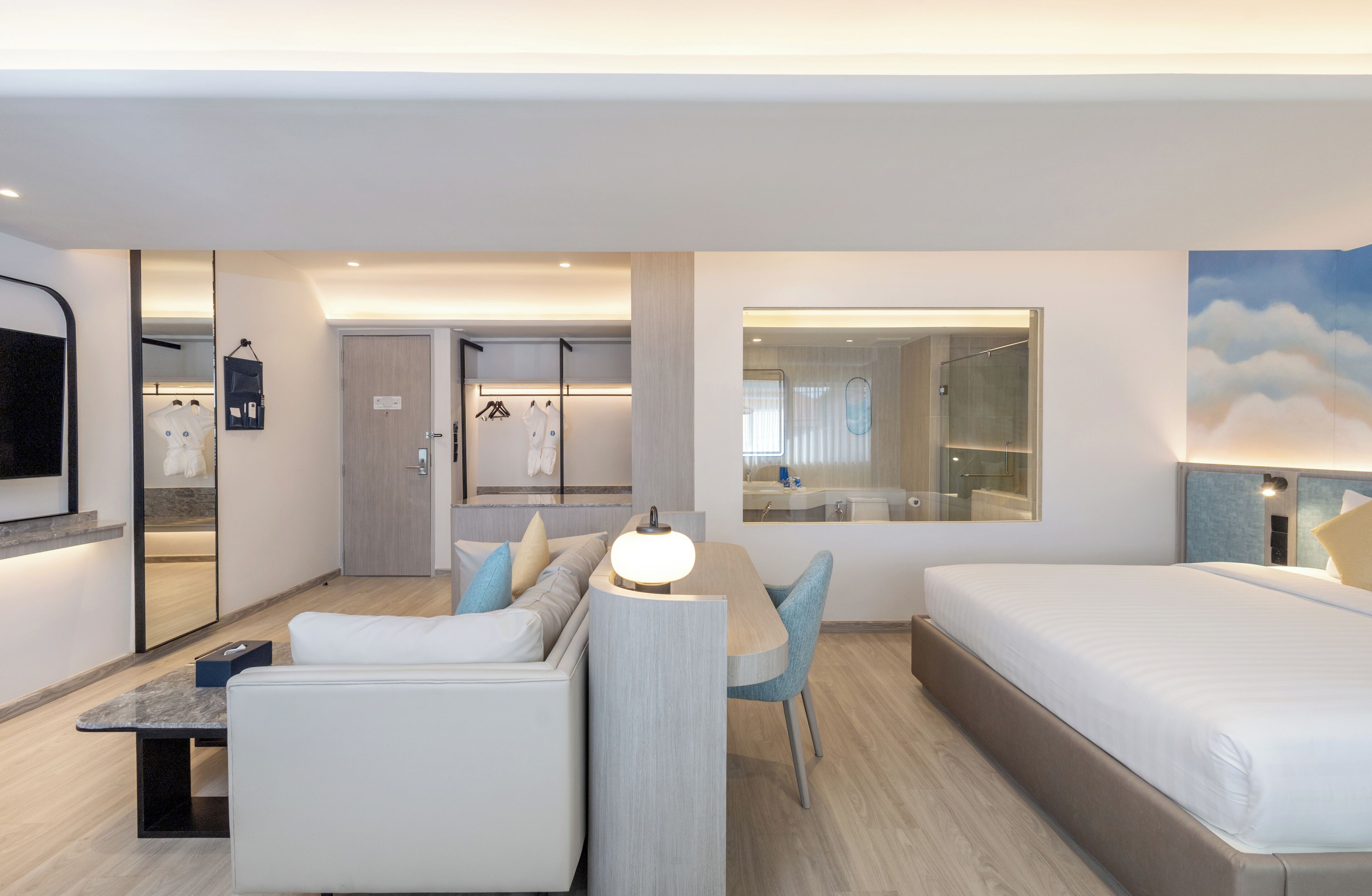 A modern hotel room with a bed, a sofa, a dining area, and a bathroom.