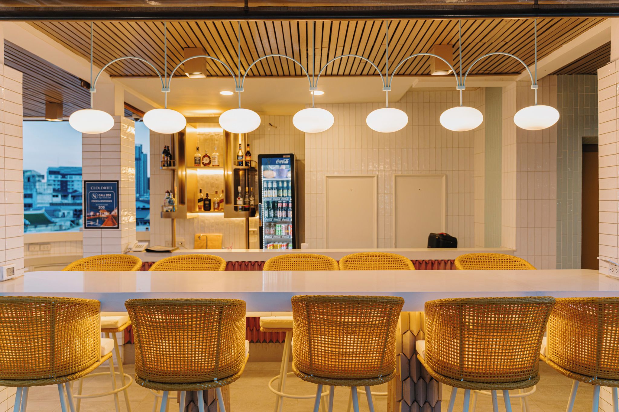A bar area with a long counter, wicker chairs, and overhead lighting.