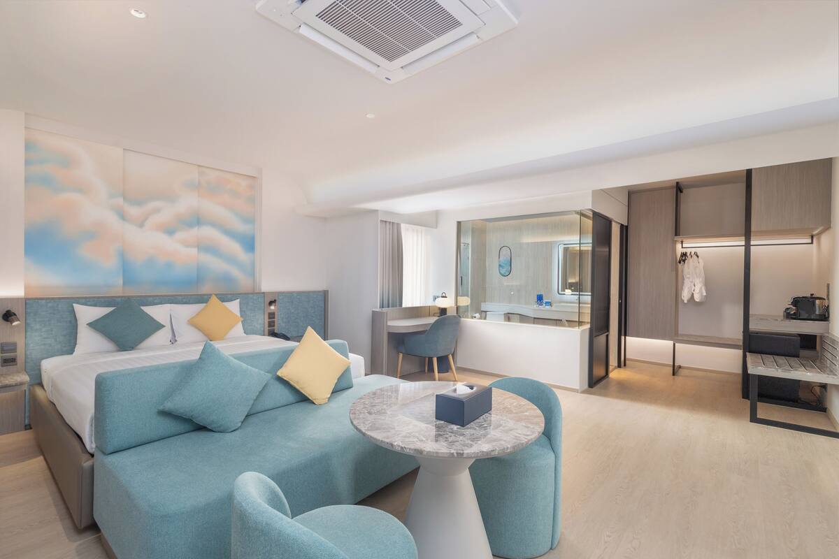 Een moderne hotelkamer met een bed, een zithoek met een tafel, een bureau en een badkamer zichtbaar door een open deur.