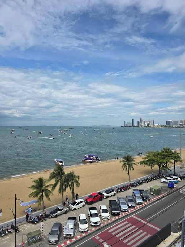 Vista de la playa con un área de estacionamiento, la playa y un horizonte urbano lejano.