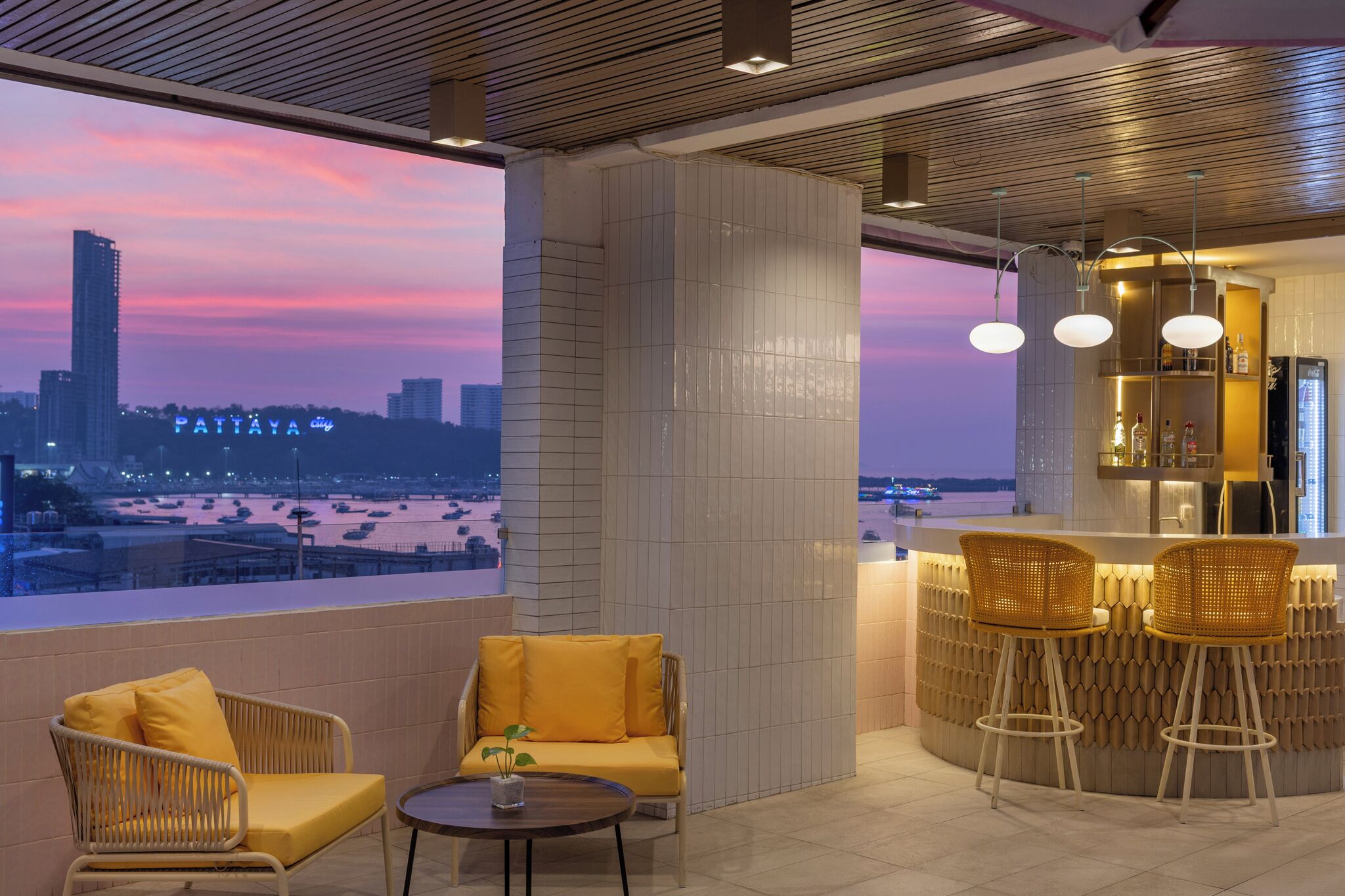 A modern interior with a view of a city skyline at dusk, featuring a bar area with stools and a seating area with chairs.