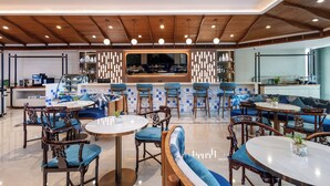 A modern restaurant with wooden ceiling beams, round tables, blue cushioned chairs, and a bar area with a large mirror. - Cloudotel Walking Street Pattaya  (Pattaya)