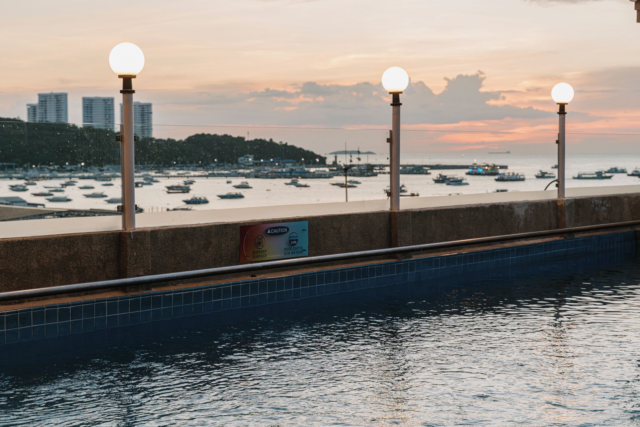 A waterfront promenade with a pool, street lamps, and a sign indicating a pool depth of 3.10 meters.