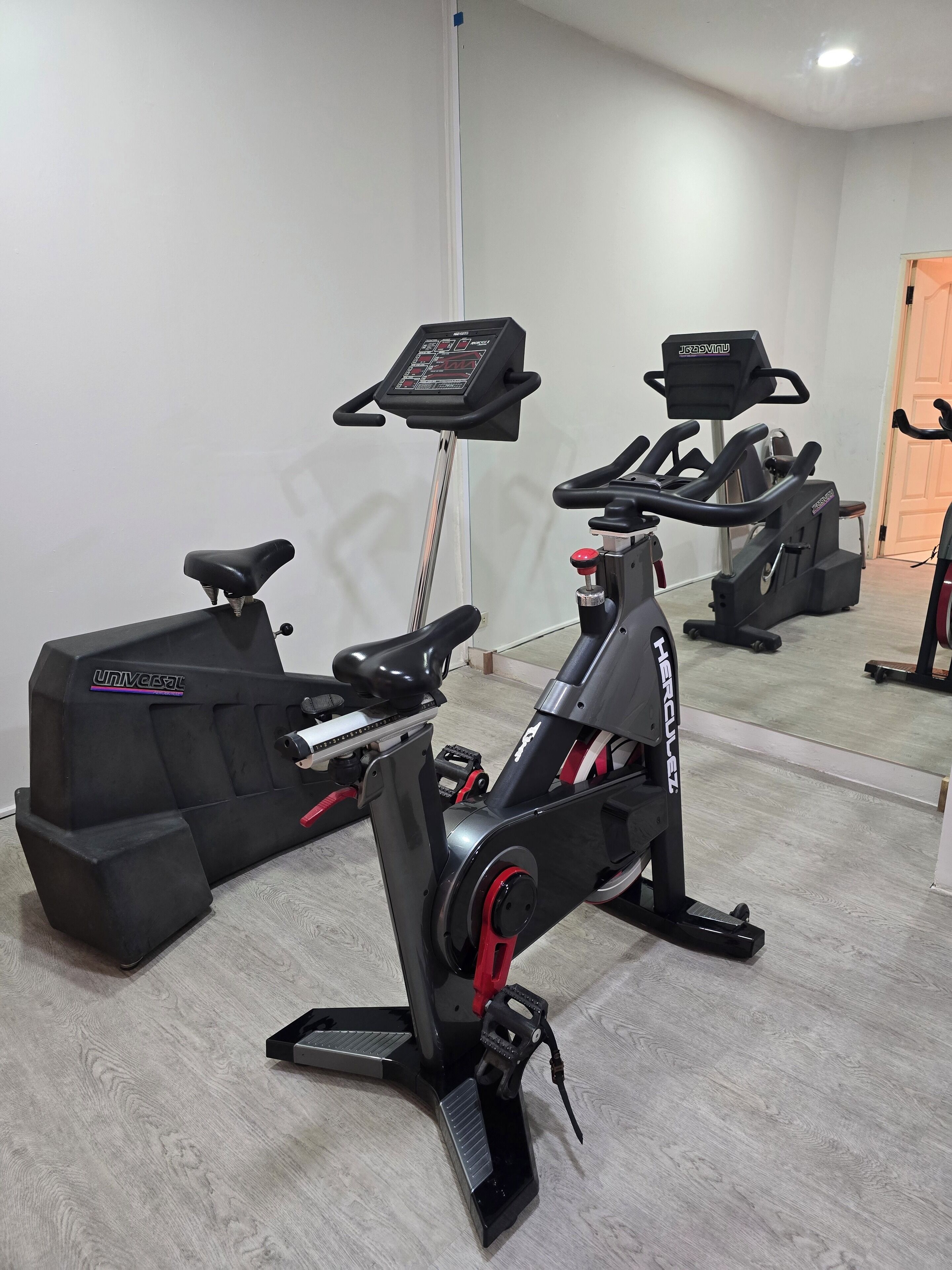A stationary bike and treadmill in a room with a wooden floor and a white wall.