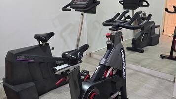 A stationary bike and treadmill in a room with a wooden floor and a white wall.
