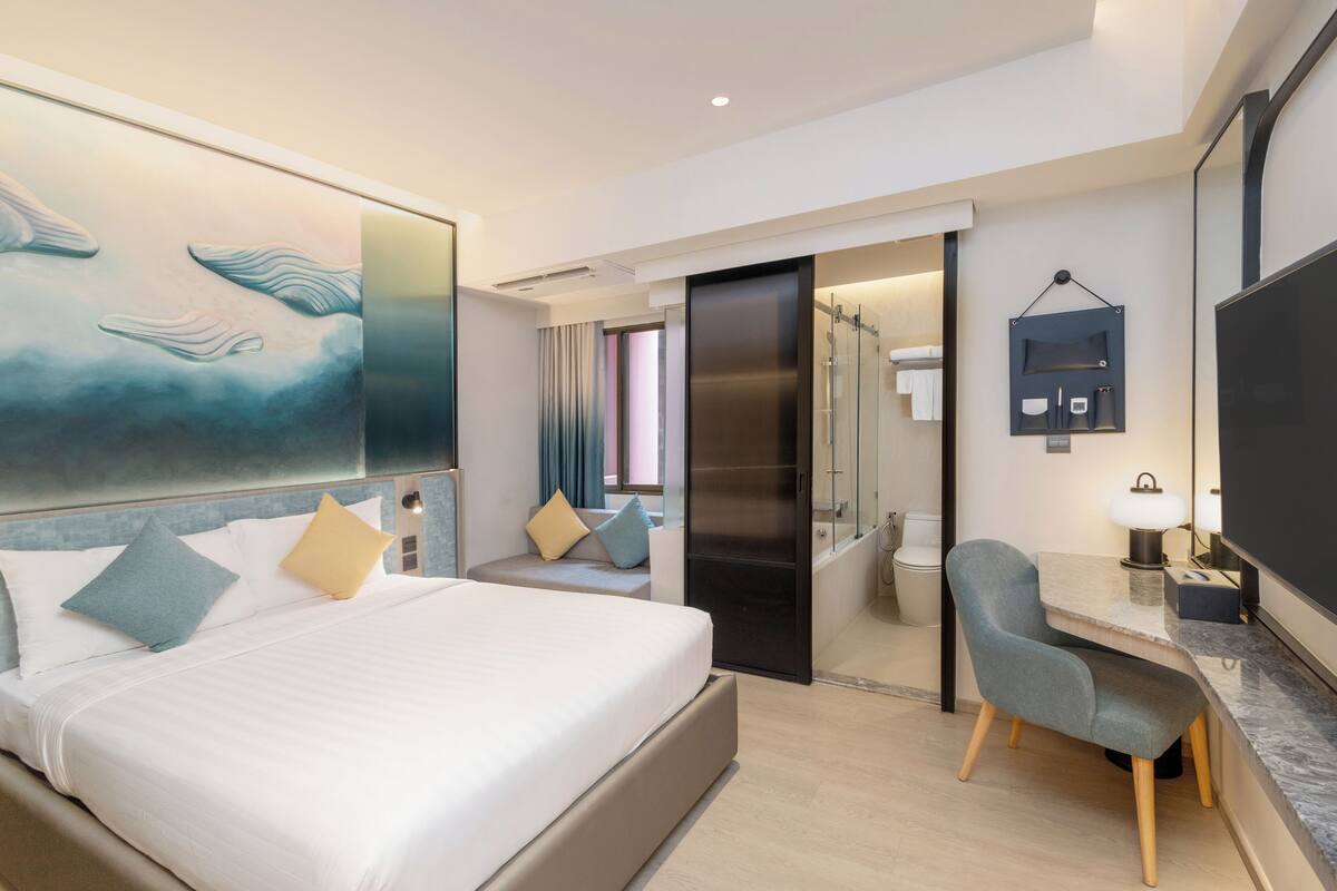 Een moderne hotelkamer met een groot bed, een bureau, een stoel en een badkamer die door een open deur zichtbaar is.