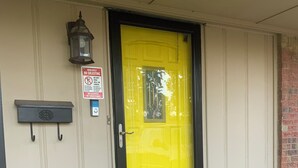 A yellow door with a black frame, a mailbox, a doorbell, and a no soliciting sign.