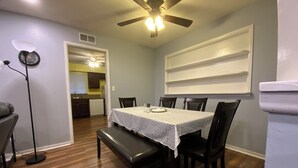 A dining area with a table set for six, wooden chairs, a ceiling fan, and a floor lamp.