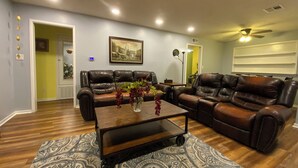 A living room with two leather sofas, a wooden coffee table with a vase of flowers, patterned rugs, and a ceiling fan.